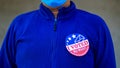 Man in mask from minority group produly holds Voted By Mail sticker during US Election closeup