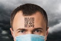 A man in a mask with a QR code on his forehead, against the background of a cloudy sky, a concept on the topic of a digital prison