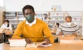 Man in mask studying in public library