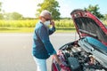 Man with mask talking on his cell phone with his car broken down Royalty Free Stock Photo