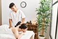 Man massaging woman back using massage gun percusion at beauty center