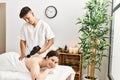 Man massaging woman back using massage gun percusion at beauty center