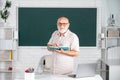 Man mature teacher. Portrait of smart senior tutor in glasses with book on the blackboard in class at high school or Royalty Free Stock Photo
