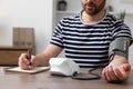 Man measuring blood pressure and writing it down into notebook in room, closeup Royalty Free Stock Photo