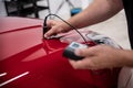 Man mechanic checking car paint thickness with electronic meter