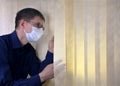 Man in a medical facial mask peeks out through the blinds Royalty Free Stock Photo