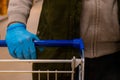 A man in medical gloves holds a grocery cart, close-up. No face visible
