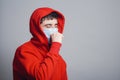 Man in medical mask coughing on gray studio background, concept of prevention viral deseases, person in red sweatshirt with