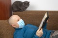 Man in a medical mask at home in quarantine because of a coronavirus epidemic reads a bible sitting on a sofa Royalty Free Stock Photo