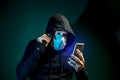 A man in a medical mask with a hood on his head looks at his smartphone