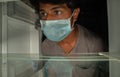 Man in a medical mask looks into empty fridge or refrigerator for food - Concept of no pantry food available during home