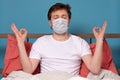 Man in medical mask meditates sitting at home on quarantine, at the bed Royalty Free Stock Photo
