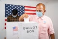 Man in medical mask placing ballot paper inside the ballot box - Concept of in person voting and people busy at polling booth at
