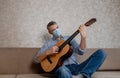a man in a medical mask plays guitar at home on the couch. Home entertainment in isolation Royalty Free Stock Photo