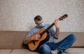 a man in a medical mask plays guitar at home on the couch. Home entertainment in isolation Royalty Free Stock Photo