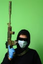 Man in a medical mask and sunglasses dressed in black clothes with a hood holds an automatic assault weapon Royalty Free Stock Photo