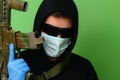 Man in a medical mask and sunglasses dressed in black clothes with a hood holds an automatic assault weapon Royalty Free Stock Photo