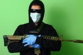 Man in a medical mask and sunglasses dressed in black clothes with a hood holds an automatic assault weapon Royalty Free Stock Photo