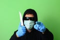 Man in a medical mask and sunglasses dressed in black clothes with a hood holds a knife in his hand Royalty Free Stock Photo