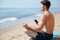 Man meditating and listening to music from smartphone on beach