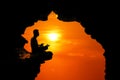 Man meditation and praying in the cave on the high cliff at sunset red sky Royalty Free Stock Photo