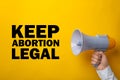 Man with megaphone involved in reproductive rights protest, closeup. Slogan Keep Abortion Legal on yellow background