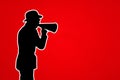 A man with a megaphone on a red background with a copy of space. Silhouette of a man in a hat and a loudspeaker. The concept of