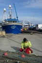 Man mending nets in Boatyard with a Fishing Boat in background, at Fraserburgh Harbour. Aberdeenshire, Scotland, UK.