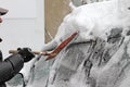 A man with a metal shovel cleans car from snow on the street after big snowstorm in the city, all cars under snow, icy roads, snow Royalty Free Stock Photo