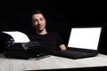 Man midway between a typewriter and laptop on black background in low key.The concept of the past and the future Royalty Free Stock Photo