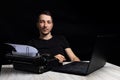 Man midway between a typewriter and laptop on black background in low key.The concept of the past and the future Royalty Free Stock Photo