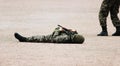Man in Military camouflage clothing and a mask lying on his back the sand with machine guns in hand during the demonstration pe