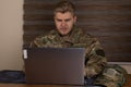 Man in military uniform using laptop in a bustling airport terminal Royalty Free Stock Photo