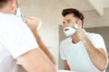 Man, mirror and shaving face with razor in bathroom for grooming, skincare or morning routine. Reflection, foam and Royalty Free Stock Photo