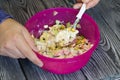 A man is mixing salad ingredients in a container. Crushed crab sticks, boiled chicken eggs, cucumber and corn