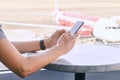 Man on mobile phone waiting for his flight at airport. Male hands holding smartphone, airplane blurry background.