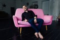 Man model sits on pink sofa in loft interior. Businessman in a black shirt and watch, blue pants.