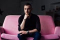 Man model sits on pink sofa in loft interior. Businessman in a black shirt and watch, blue pants. Royalty Free Stock Photo