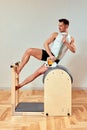 A man with a model of the spine in his hands during Pilates on the reformer. A young man shows how the spine bends when
