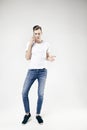 Man model talking by mobile phone wearing jeans and white t-shirt, full-length standing and showing something by left hand