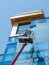 Man with mop washing a blue glass wall from autotower or aerial work platform on a sunny summer day. Real people and city life.