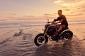 Man And Motorcycle On Ocean Beach At Beautiful Tropical Sunset. Handsome Biker On Motorbike.