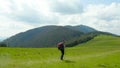 A man in the mountains with a backpack on his back walks along a grassy slope Royalty Free Stock Photo