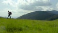 A man in the mountains with a backpack on his back walks along a grassy slope