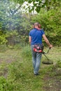 Man mowing grass with electric or petrol lawn trimmer in backyard. The gardener mows weeds. Royalty Free Stock Photo