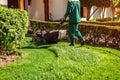 Man mowing the grass with a lawn mower by hotel. Worker cuts the lawn in summer garden