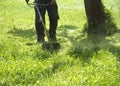 The man mowing green wild grass field using brush cutter mower or power tool string lawn trimmer Royalty Free Stock Photo