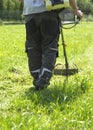 The man mowing green wild grass field using brush cutter mower or power tool string lawn trimmer Royalty Free Stock Photo