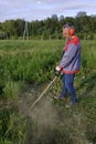 Man mows the grass with a trimmer, tall grass in a meadow, handmade in the garden Royalty Free Stock Photo