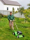 man mows a spring green lawn with dandelions in the garden. trimming dandelions and other weeds in the yard. an Royalty Free Stock Photo